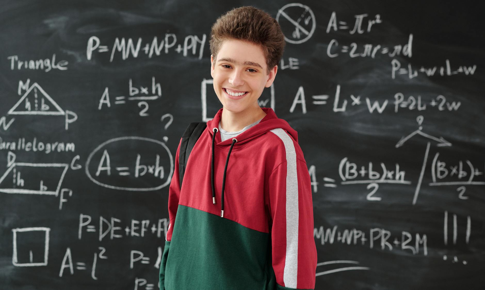 boy in red jacket standing in front of the blackboard